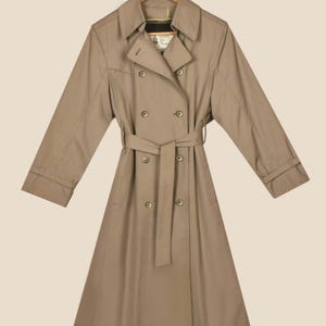 K&ouml;nnte beinhalten: Ein beiger Trenchcoat mit doppelreihigem Verschluss, G&uuml;rtel und langen &Auml;rmeln.