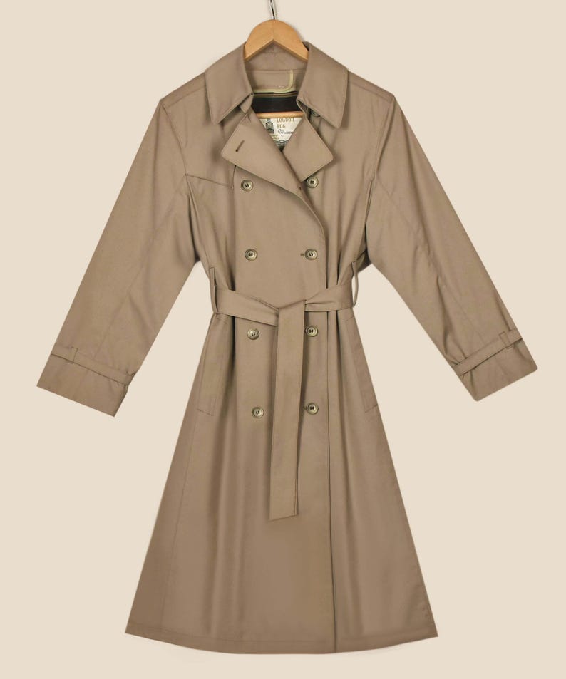 K&ouml;nnte beinhalten: Ein beiger Trenchcoat mit doppelreihigem Verschluss, G&uuml;rtel und langen &Auml;rmeln.