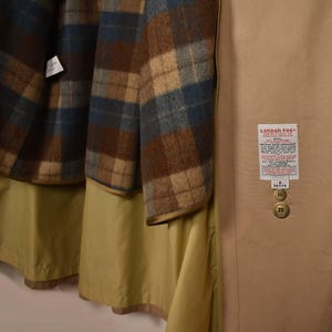 K&ouml;nnte beinhalten: Ein beiger London Fog Mantel mit einem karierten Futter. Der Mantel hat ein Etikett mit der Aufschrift "London Fog" und "Petite" Gr&ouml;&szlig;e 8.