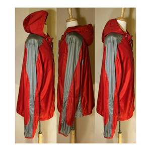 Op de afbeelding: Een rode en grijze hooded jas met een ritssluiting. De jas heeft een sportief ontwerp met een contrasterend kleurenpaneel op de mouwen.