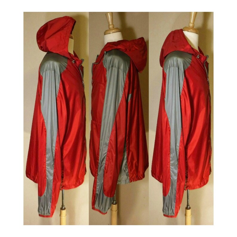 Op de afbeelding: Een rode en grijze hooded jas met een ritssluiting. De jas heeft een sportief ontwerp met een contrasterend kleurenpaneel op de mouwen.