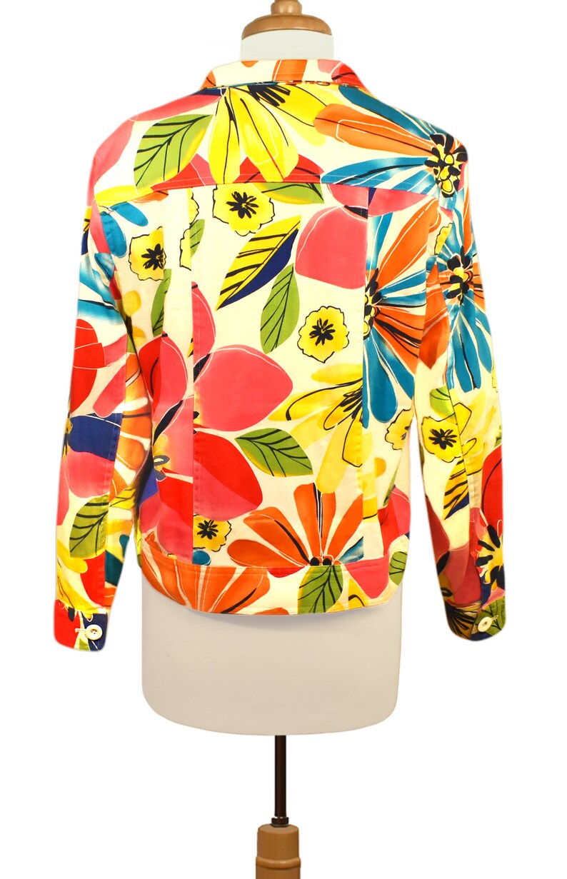 May include: A white denim jacket with a colorful floral print. The print features large flowers in shades of pink, red, yellow, blue, and green.