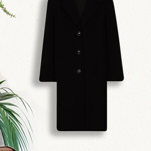 May include: A black long-sleeved coat with a collar and four buttons down the front. The coat is hanging on a wooden hanger against a white background.
