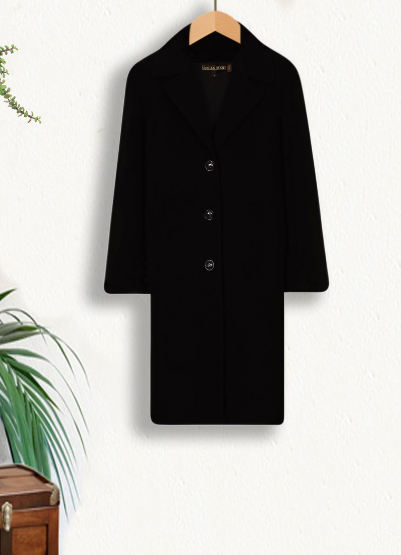 May include: A black long-sleeved coat with a collar and four buttons down the front. The coat is hanging on a wooden hanger against a white background.