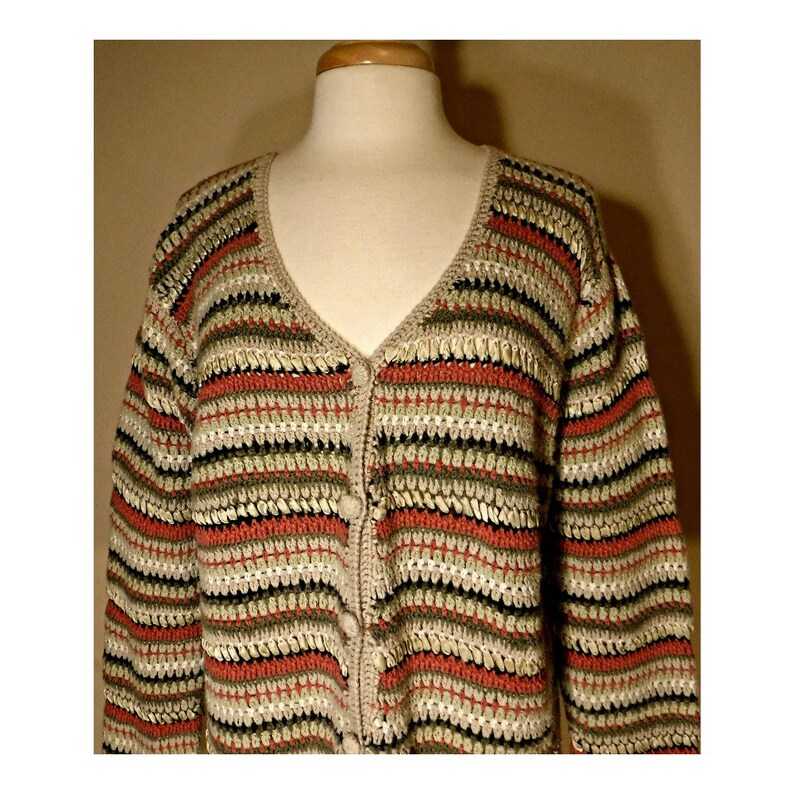 May include: A striped crocheted cardigan with a v-neck and button closure. The cardigan is made in shades of beige, green, and red.