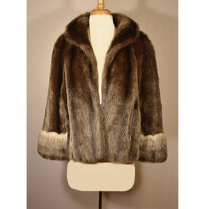 Peut inclure: Une veste en fausse fourrure marron avec une bordure blanche autour du col et des poignets. La veste est ouverte &agrave; l'avant et est expos&eacute;e sur un mannequin.