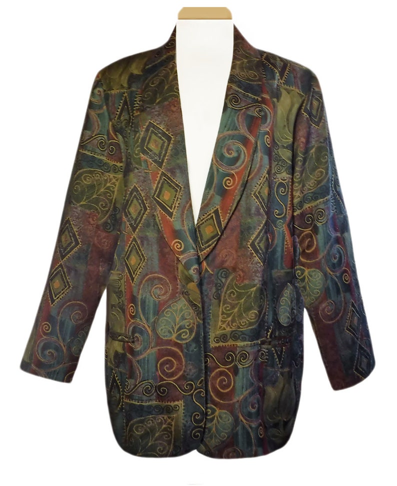 May include: A patterned blazer in shades of green, brown, and blue. The blazer features a unique design with diamond and swirl patterns. It has a classic lapel and two front pockets. The blazer is displayed on a white mannequin.