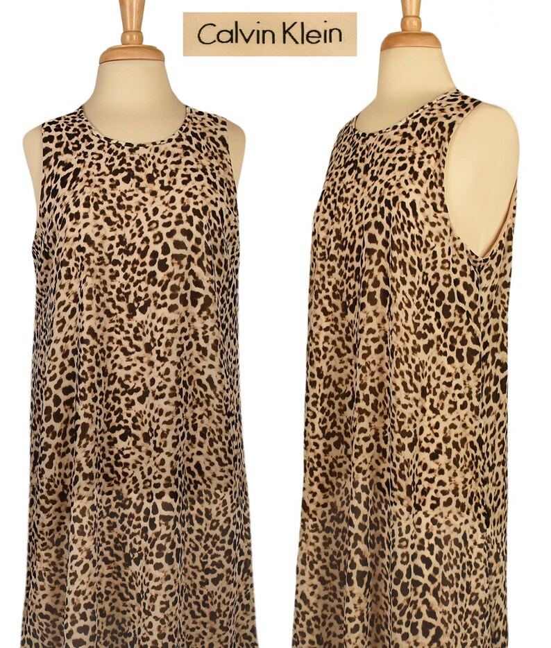 May include: A sleeveless, knee-length dress with a leopard print pattern. The dress is made of a sheer fabric and has a round neckline. The dress is on a mannequin and the brand name "Calvin Klein" is visible at the top of the image.