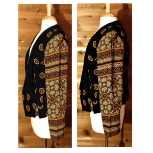 May include: A black and gold patterned jacket with a V-neck and long sleeves. The jacket has a geometric pattern with a black background and gold accents.