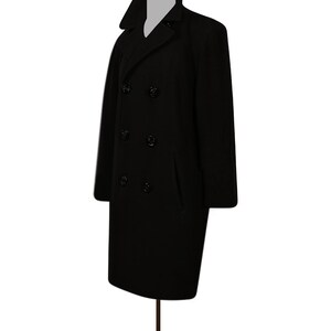 K&ouml;nnte beinhalten: Ein schwarzer Peacoat mit doppelreihigem Verschluss und vier schwarzen Kn&ouml;pfen. Der Mantel hat zwei Pattentaschen auf der Vorderseite.