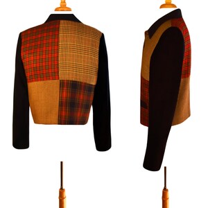 May include: A black cropped jacket with a patchwork design. The patchwork is made of four different plaid fabrics in shades of red, brown, and black.