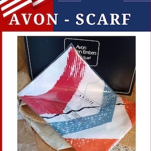 Op de afbeelding: Een gevouwen sjaal in een doorzichtige plastic zak met een witte achtergrond en abstracte rode en blauwe penseelstreekpatronen. Het Avon-logo staat op de verpakking, die ook veiligheidstekst en de tekst Avon Autumn Embers Scarf bevat.