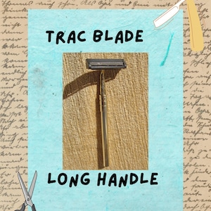 Puede incluir: Se muestra una maquinilla de afeitar Trac Blade vintage con un mango largo. La maquinilla tiene un cabezal negro y un mango dorado. El texto "TRAC BLADE" y "LONG HANDLE" están escritos encima y debajo de la maquinilla.