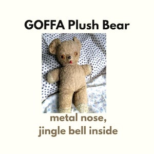 Puede incluir: Un oso de peluche color canela con ojos naranjas, una pequeña lengua roja y una nariz de metal. El texto GOFFA Plush Bear y metal nose, jingle bell inside aparece impreso sobre y bajo el oso. El oso tiene patas claras y orejas redondeadas.