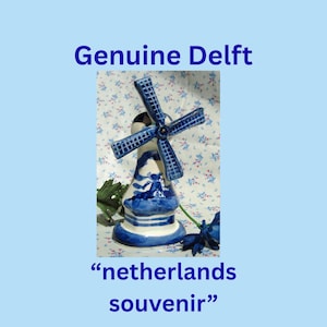 May include: A blue and white ceramic windmill figurine with a windmill design. The figurine has a blue and white color scheme and the text "Genuine Delft" and "netherlands souvenir" are visible.