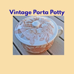 Könnte beinhalten: Vintage Nachttopf mit floralem Design in Pfirsich- und Weißtönen. Der Deckel hat einen weißen Knopf und einen Griff. Der Text "Vintage Porta Potty" wird in Blau angezeigt.