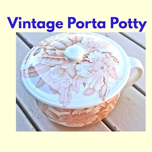 May include: A vintage porta potty featuring a round lid and a side handle. The exterior and lid are decorated with a brown floral pattern on a white background. The text "Vintage Porta Potty" is printed in blue above the object.