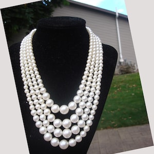 May include: A multi-strand pearl necklace displayed on a black bust. The necklace features graduated sizes of round, white pearls. The strands cascade down, creating a layered effect, with the largest pearls at the bottom.