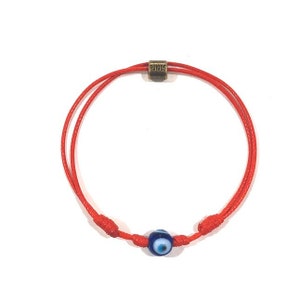 Puede incluir: Pulsera de cuerda roja con un amuleto de ojo turco azul y una cuenta dorada con la palabra "RUIGOS" grabada.