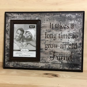 May include: A rectangular photo frame with a 5x7 inch photo opening. The frame has a distressed gray and black finish with the text "It takes a long time to grow an old Friend". The frame is made of wood.