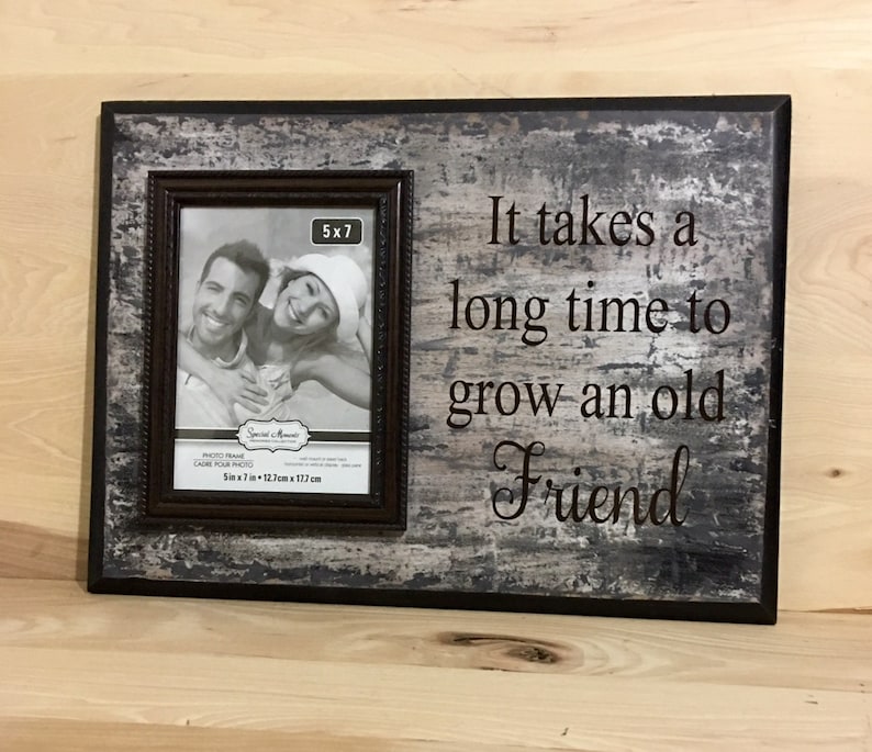 May include: A rectangular photo frame with a 5x7 inch photo opening. The frame has a distressed gray and black finish with the text "It takes a long time to grow an old Friend". The frame is made of wood.