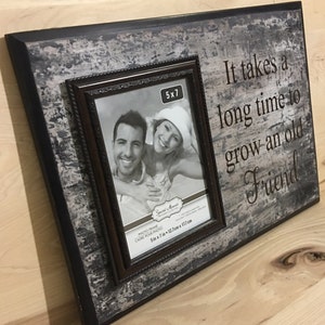 May include: A rustic wooden photo frame with a distressed gray and black finish. It holds a 5x7 inch photo and features the quote, "It takes a long time to grow an old Friend."