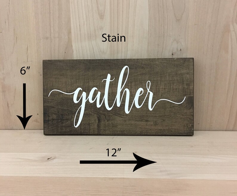 May include: A wooden sign with the word "gather" in white lettering on a dark brown stained background. The sign measures 12 inches wide and 6 inches tall.