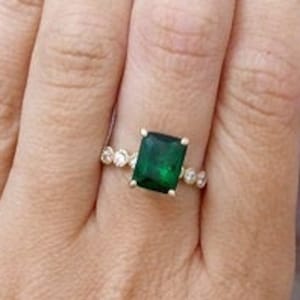 May include: A gold ring with a large emerald green square gemstone surrounded by smaller clear gemstones.