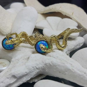 May include: Gold snake ring with two blue opal stones. The snake is coiled around the stones.