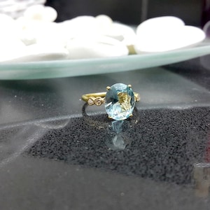 May include: A gold ring featuring a large oval aquamarine gemstone and smaller diamonds set in the band.