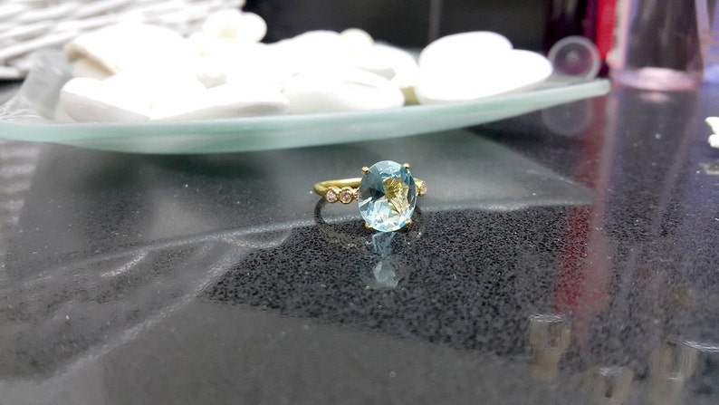 May include: A gold ring featuring a large oval aquamarine gemstone and smaller diamonds set in the band.
