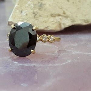 May include: A gold ring featuring a large oval black gemstone and three smaller round white gemstones set into the band.