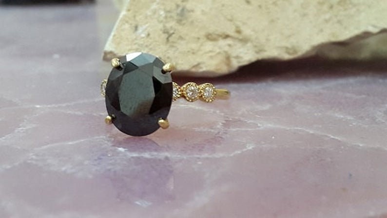 May include: A gold ring featuring a large oval black gemstone and three smaller round white gemstones set into the band.
