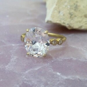 May include: A gold ring featuring a large oval-shaped clear gemstone and smaller clear gemstones set in the band.