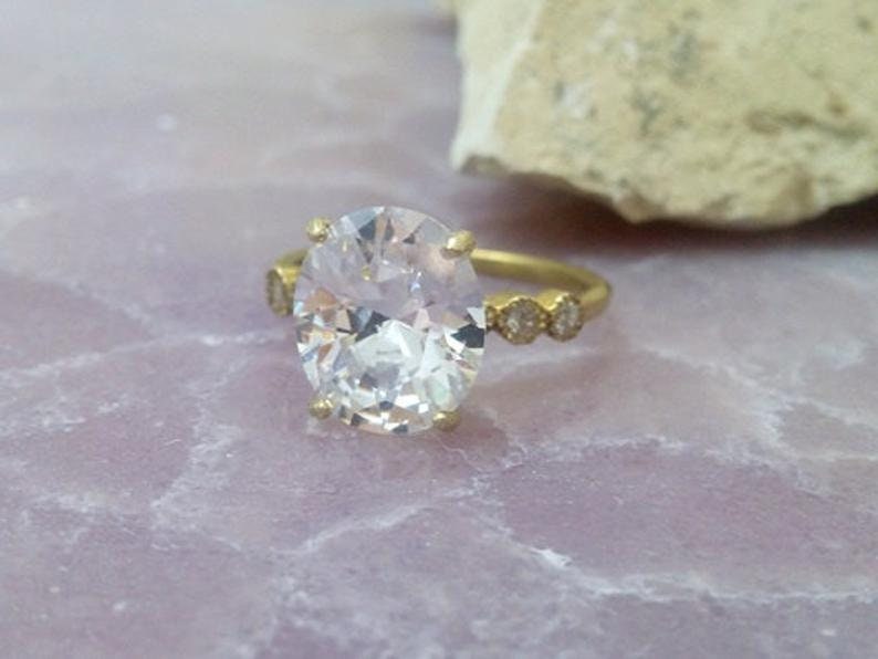 May include: A gold ring featuring a large oval-shaped clear gemstone and smaller clear gemstones set in the band.