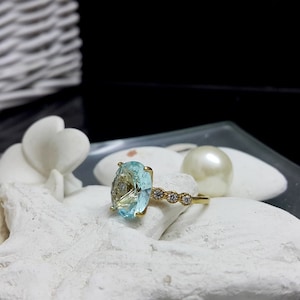 May include: A gold ring featuring a large oval blue gemstone and smaller clear gemstones set into the band.