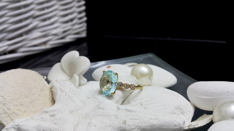 May include: A gold ring featuring a large oval blue gemstone and smaller clear gemstones set into the band.