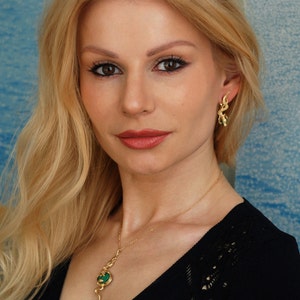 May include: A woman wearing a black top with a gold necklace and earrings. The necklace and earrings feature green stones and gold accents.