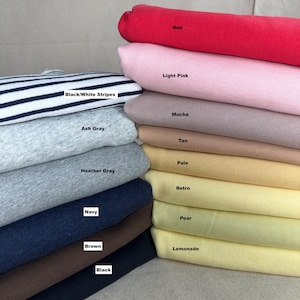Puede incluir: Una pila de telas dobladas en varios colores, incluyendo rojo, rosa claro, moca, beige, amarillo pálido, amarillo retro, verde pera y amarillo limón. Otros colores incluyen rayas negras/blancas, gris ceniza, gris jaspeado, azul marino, marrón y negro. Cada tela tiene una etiqueta con su nombre de color.