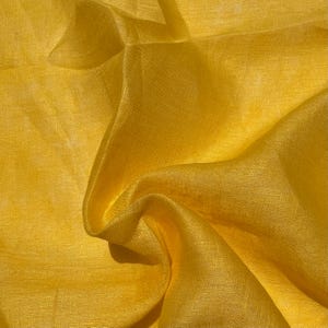 Puede incluir: Primer plano de una tela amarilla vibrante con pliegues suaves y un brillo sutil. El material parece ligero y fluido, lo que sugiere que podría usarse para ropa o fines decorativos. El color es un amarillo rico y soleado.