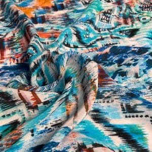 Puede incluir: Tejido abstracto con un patrón vibrante en tonos de azul, turquesa, naranja y negro. El diseño presenta patrones similares a pinceladas y formas geométricas, creando un textil dinámico y artístico.