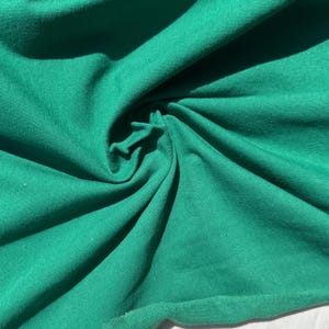 Pode incluir: Close-up de um tecido verde vibrante, torcido para criar um padrão texturizado. A superfície do tecido é lisa, com sombras sutis que adicionam profundidade. A cor é um verde rico e saturado, sugerindo um material têxtil.