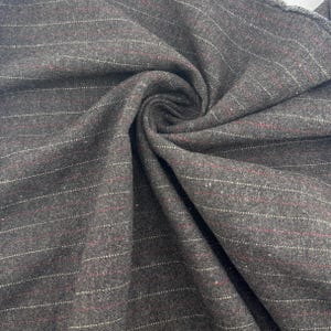 Puede incluir: Primer plano de una tela gris oscuro con un sutil patrón de rayas finas. La tela tiene finas rayas blancas y rojas que recorren el material verticalmente. La tela está doblada y drapeada, mostrando su textura y caída.