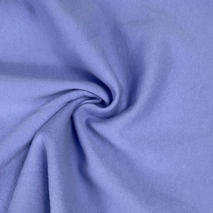Pode incluir: Close-up de um redemoinho de tecido azul-arroxeado claro. O tecido tem uma textura macia e fosca e é densamente tecido. A cor é um azul-púrpura pálido e suave, com variações sutis de tom devido às dobras e sombras.
