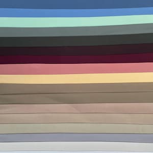Puede incluir: Una muestra de colores con una variedad de muestras de tela en una gama de colores lisos. Las muestras incluyen tonos de azul, verde, gris, rosa y beige. La tela parece suave y posiblemente sea un material ligero.