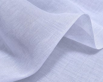 Puede incluir: Una pieza de tela de color lavanda claro con una textura tejida visible. El material está drapeado en pliegues suaves y fluidos, creando luces y sombras en la superficie que resaltan el tejido fino y consistente del material textil.