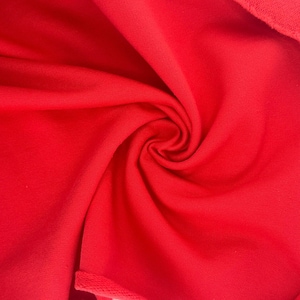 Pode incluir: Close-up de um tecido vermelho vibrante com uma textura macia. O material é fortemente enrolado, criando um padrão em espiral. O tecido parece ser um material de malha ou jersey, adequado para projetos de vestuário ou decoração de casa.