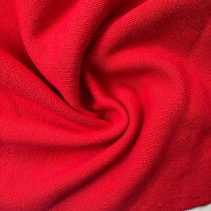 Pode incluir: Close-up de um tecido vermelho vibrante, provavelmente malha ou jersey. A textura é macia e ligeiramente canelada, com dobras e sombras visíveis que adicionam profundidade. A cor é um vermelho sólido e brilhante.