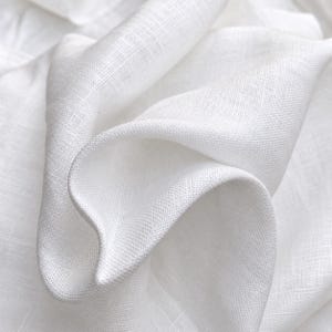 May include: A piece of white fabric with a visible woven texture and a natural, slightly irregular weave pattern. The material is draped in soft, flowing folds, highlighting the matte finish and the crisp, clean appearance of the white textile.