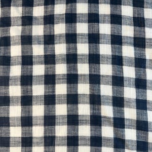 Puede incluir: Primer plano de una tela con un patrón de cuadros clásico. El diseño presenta una cuadrícula de cuadrados azul marino y blancos alternados. La tela parece ligera y ligeramente texturizada, lo que sugiere que podría usarse para ropa o decoración del hogar.